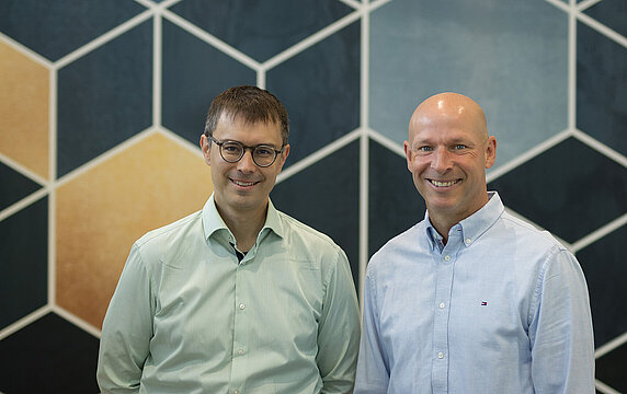 Die beiden Forscher von der MUHS vor Wand mit geometrischen Mustern.